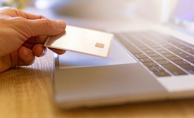 hand holding a credit card in front of a laptop